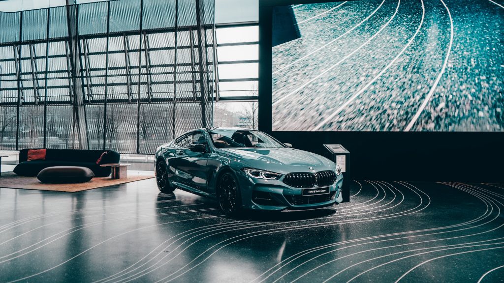 Blau Grüner Bmw in einer Halle vor einer Leinwand mit Wellen-förmigen Linien.